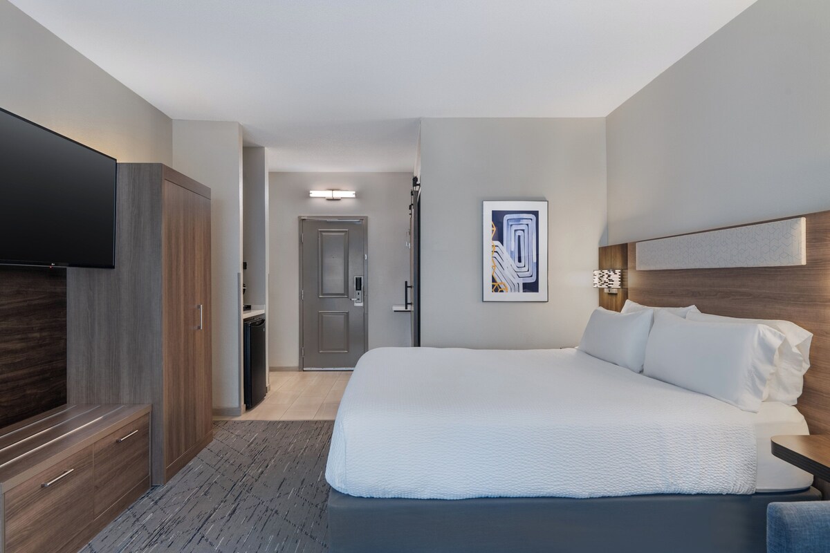 Une chambre d’hôtel moderne dotée d’un grand lit, d’un téléviseur à écran plat, d’une armoire et d’un tableau abstrait encadré accroché au mur.
