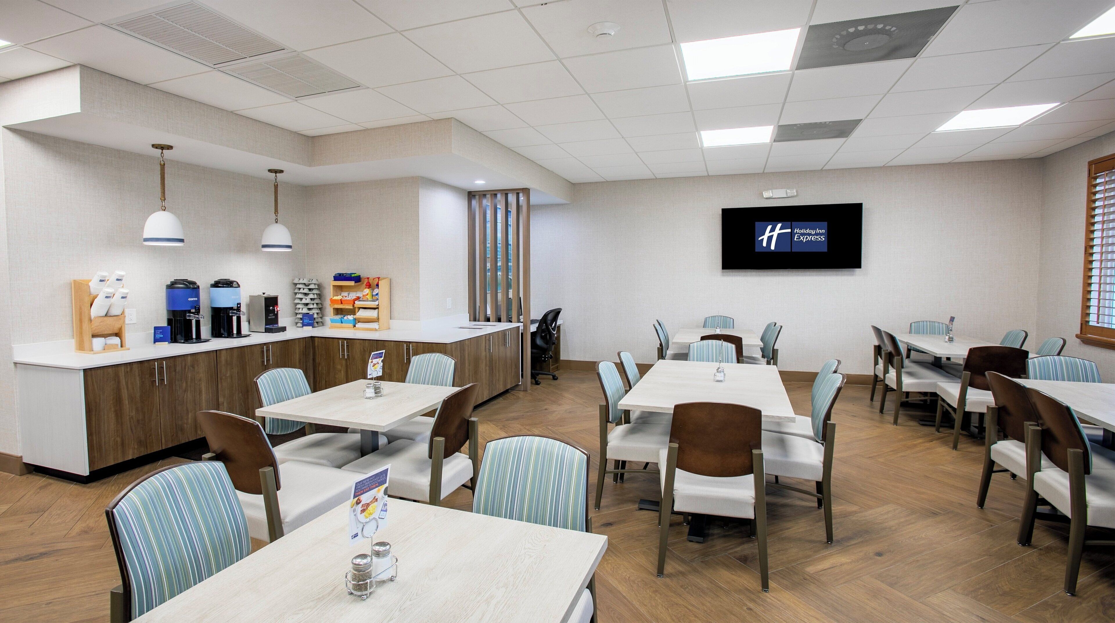 Une salle de conférence d’hôtel équipée de tables, de chaises, d’un coin café et d’un écran de télévision affichant le logo de Holiday Inn Express.