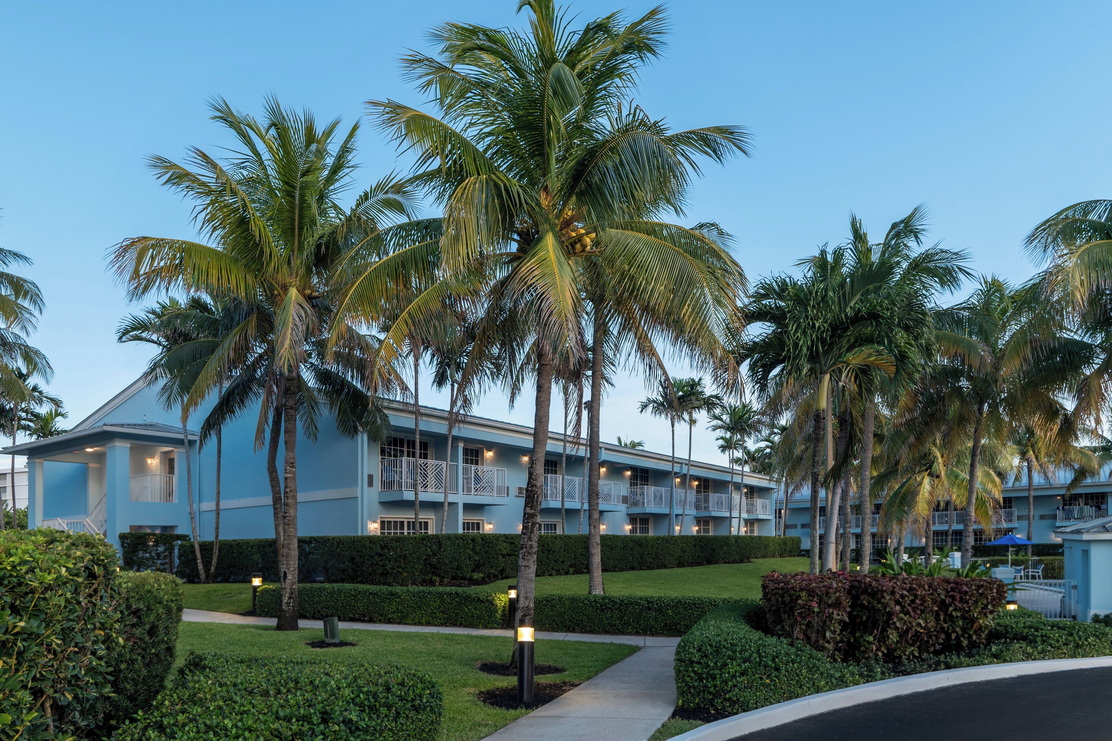 A resort with a blue building, palm trees, and a well-maintained garden.