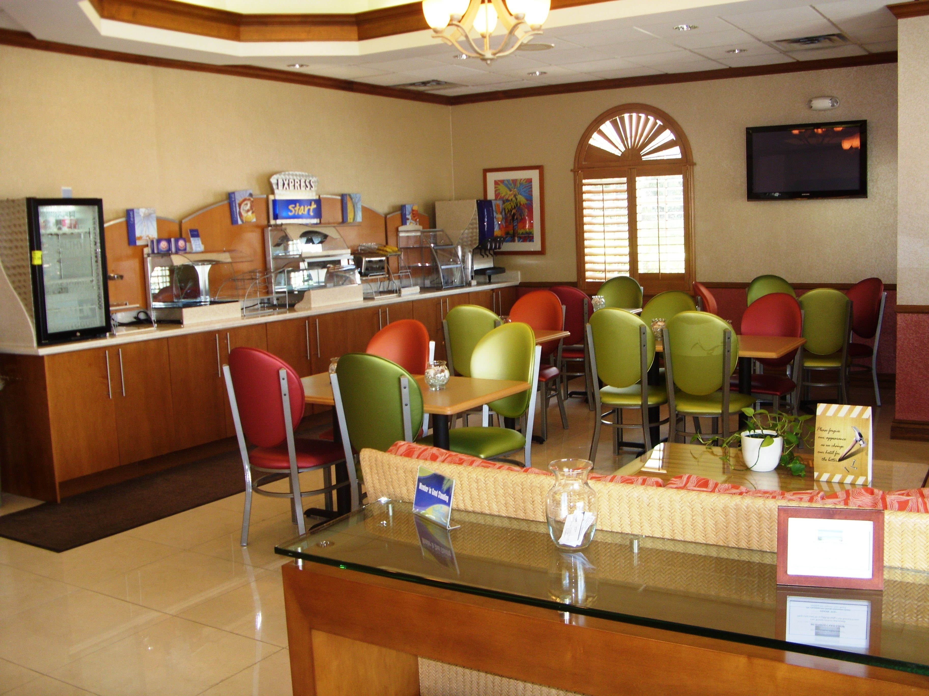 A restaurant with a counter, various chairs, a television, and a window with blinds.