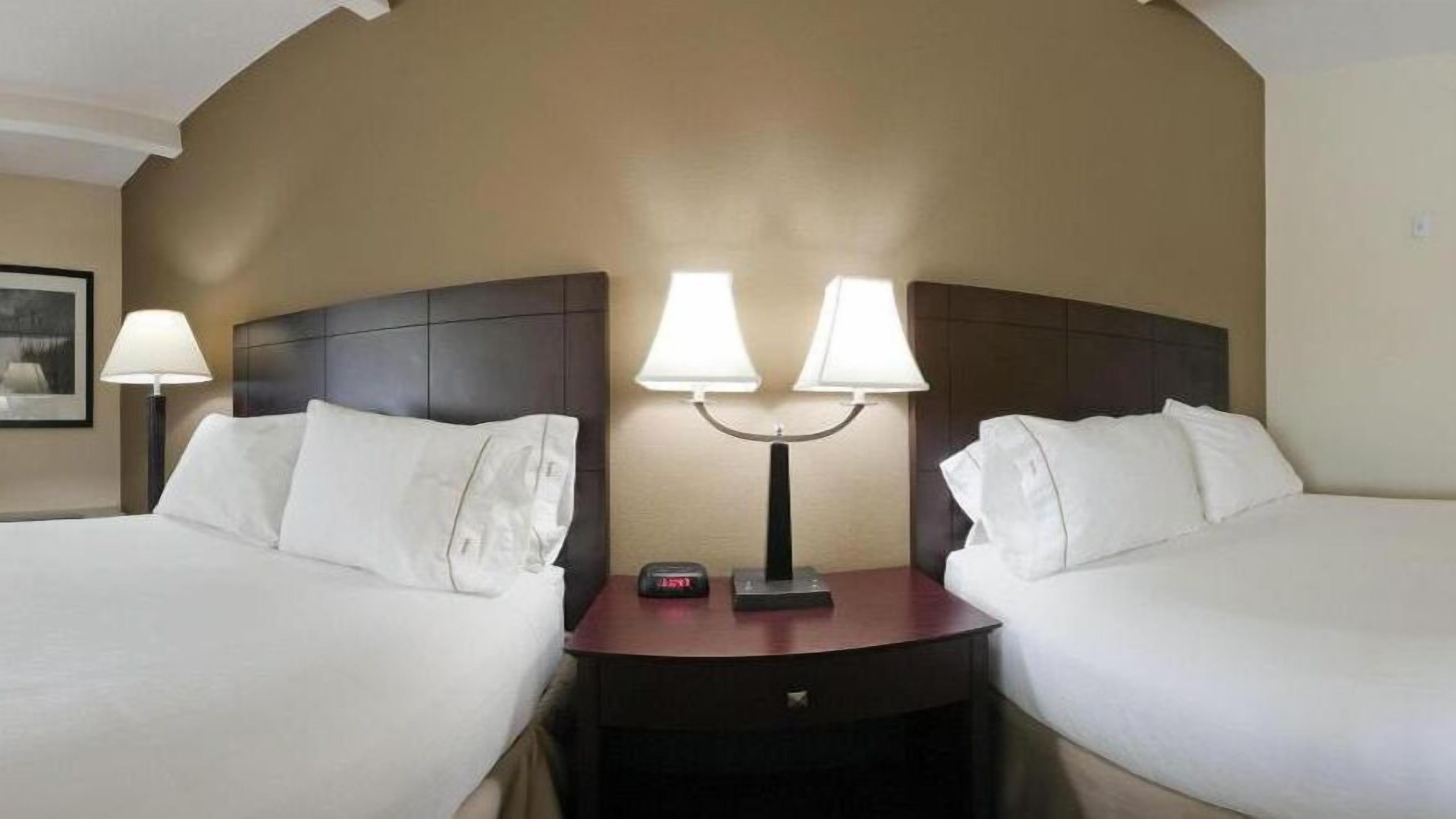 Habitación de hotel con dos camas, una mesita de noche con una lámpara y un reloj.
