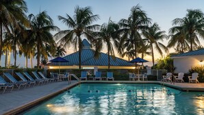 Une piscine entourée de chaises longues et de parasols, bordée de palmiers et d’un bâtiment doté d’un toit bleu.