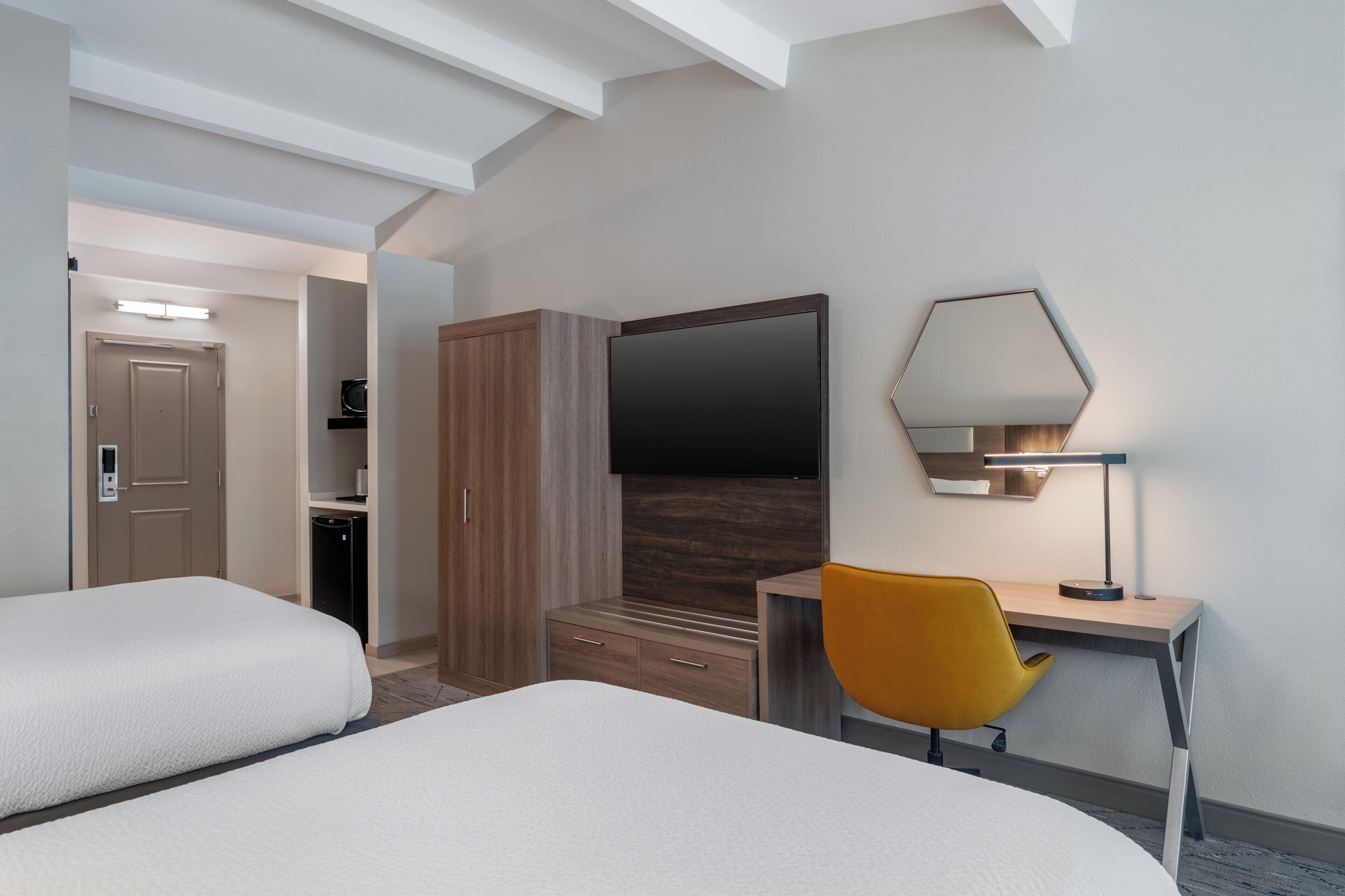 Une chambre d’hôtel avec deux lits, un bureau avec une chaise, une télévision, un miroir et une lampe.