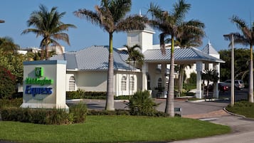 A hotel with a sign indicating it's a Holiday Inn Express, surrounded by palm trees and a parking lot.