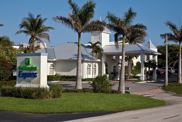 Un hotel con un letrero que indica que es un Holiday Inn Express, rodeado de palmeras y un estacionamiento.