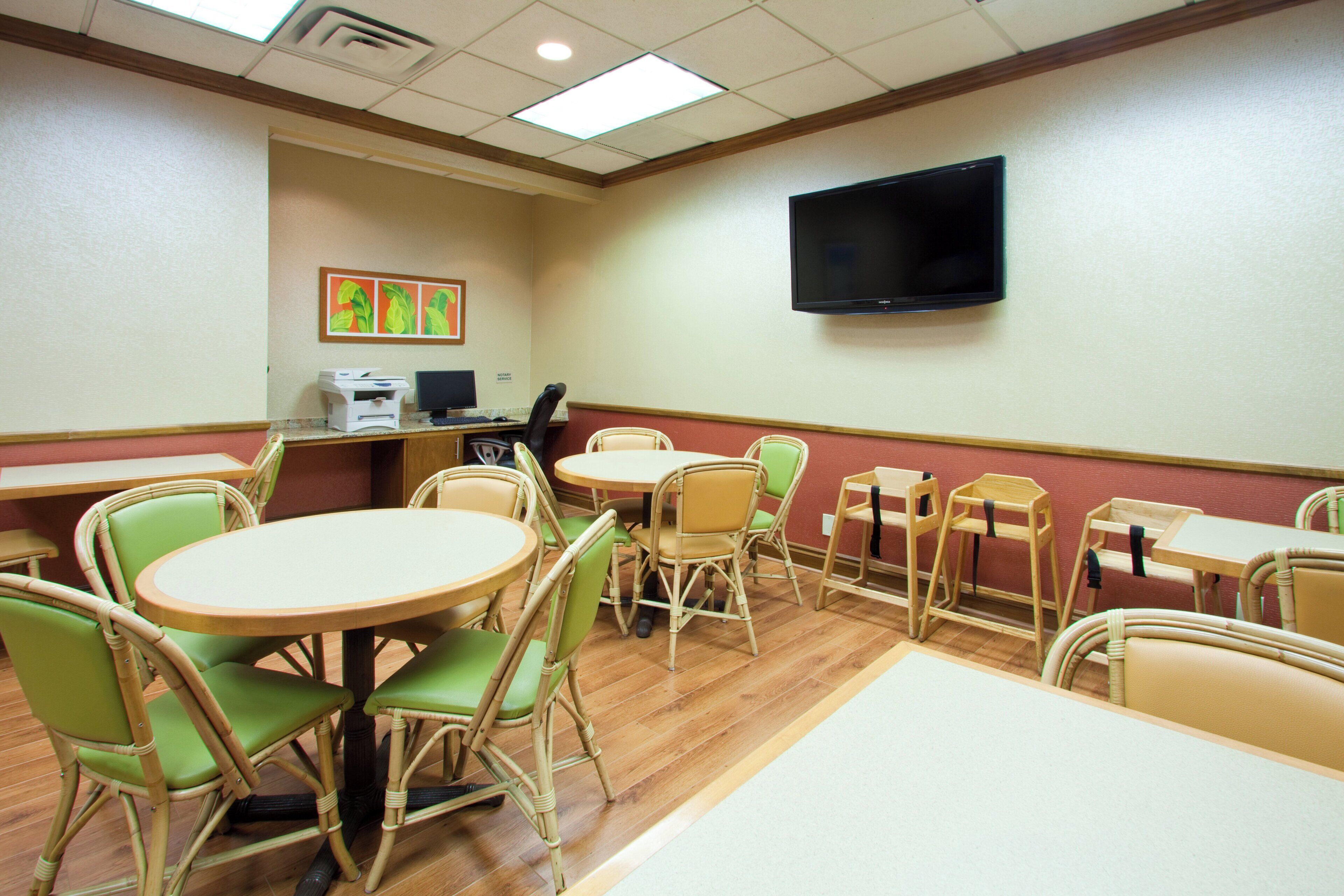 A conference room with round tables and chairs, a flat-screen TV mounted on the wall, and a printer on a desk.