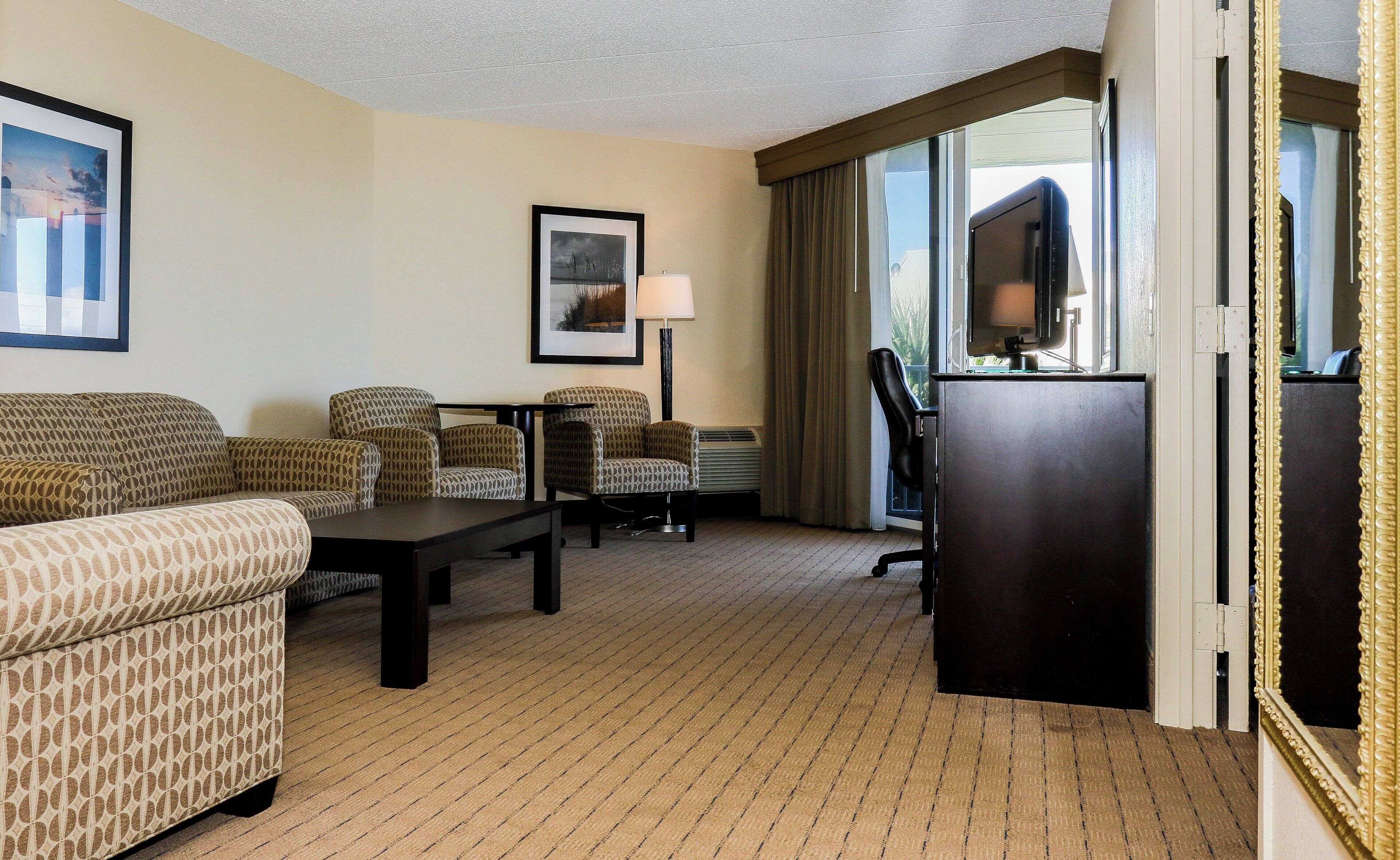 A hotel room with a sofa, two armchairs, a desk, a lamp, and a television.