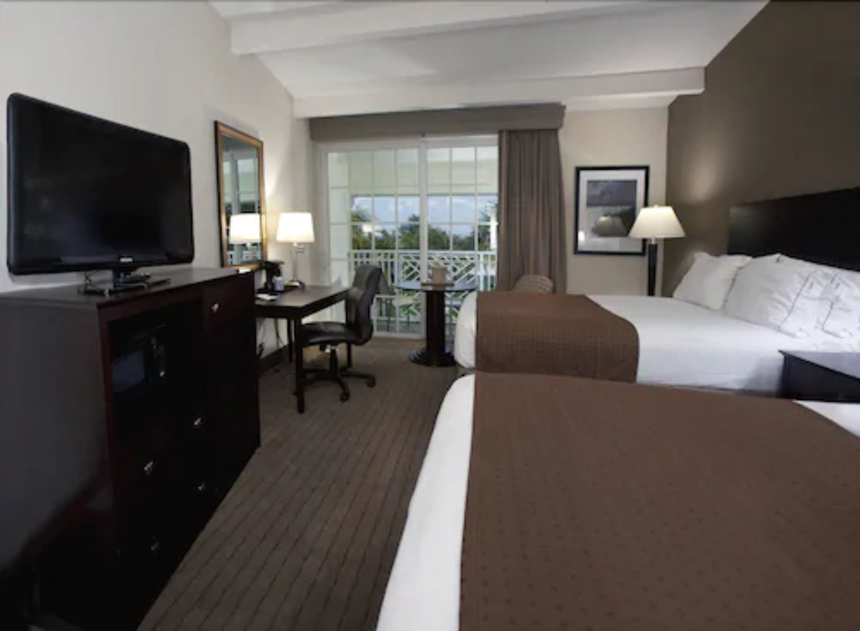 A hotel room with a bed, a desk, a chair, a TV, and a window with a view.