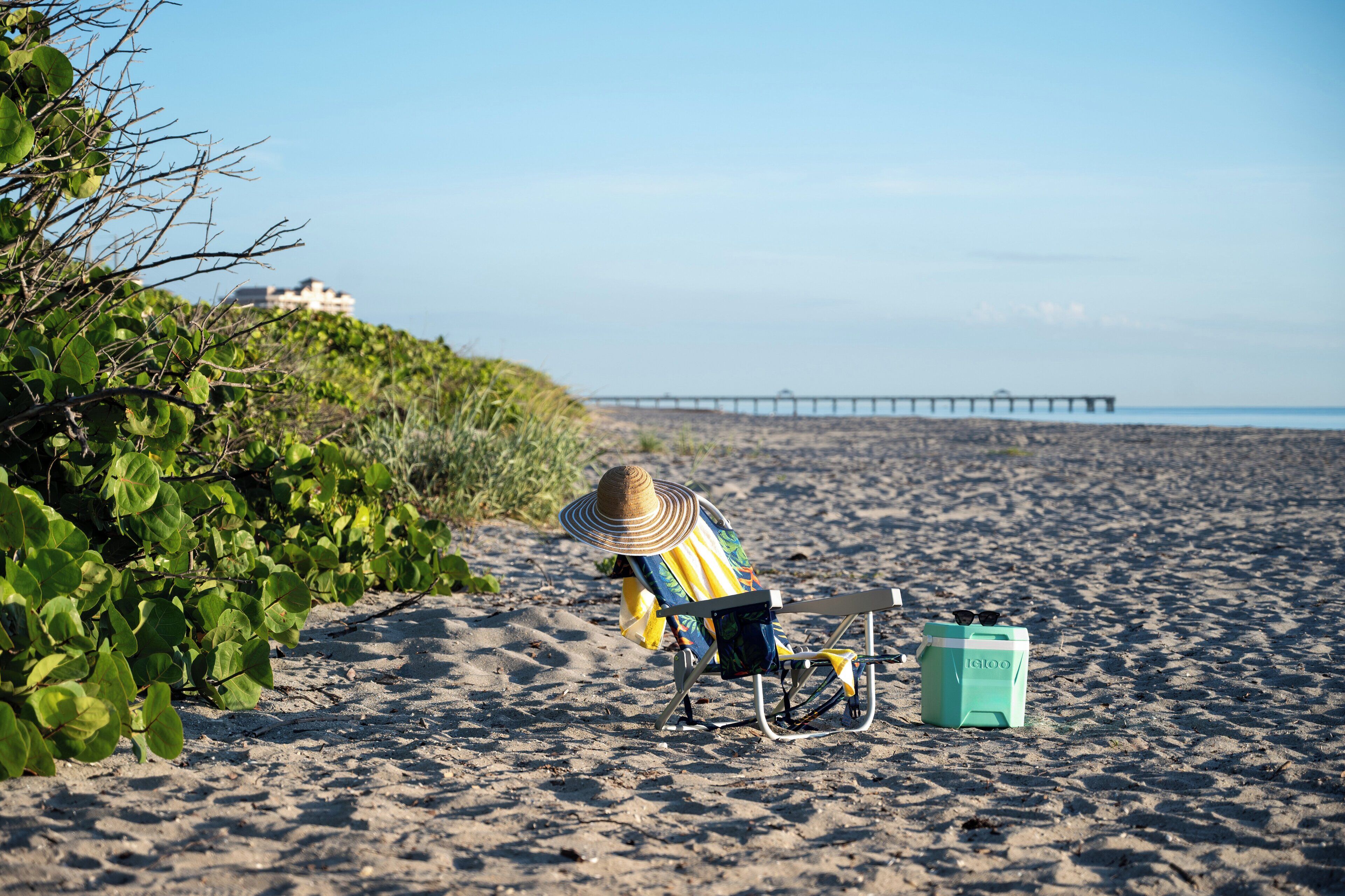 A beach scene with a person sitting on a beach chair, a cooler, and a beach umbrella.