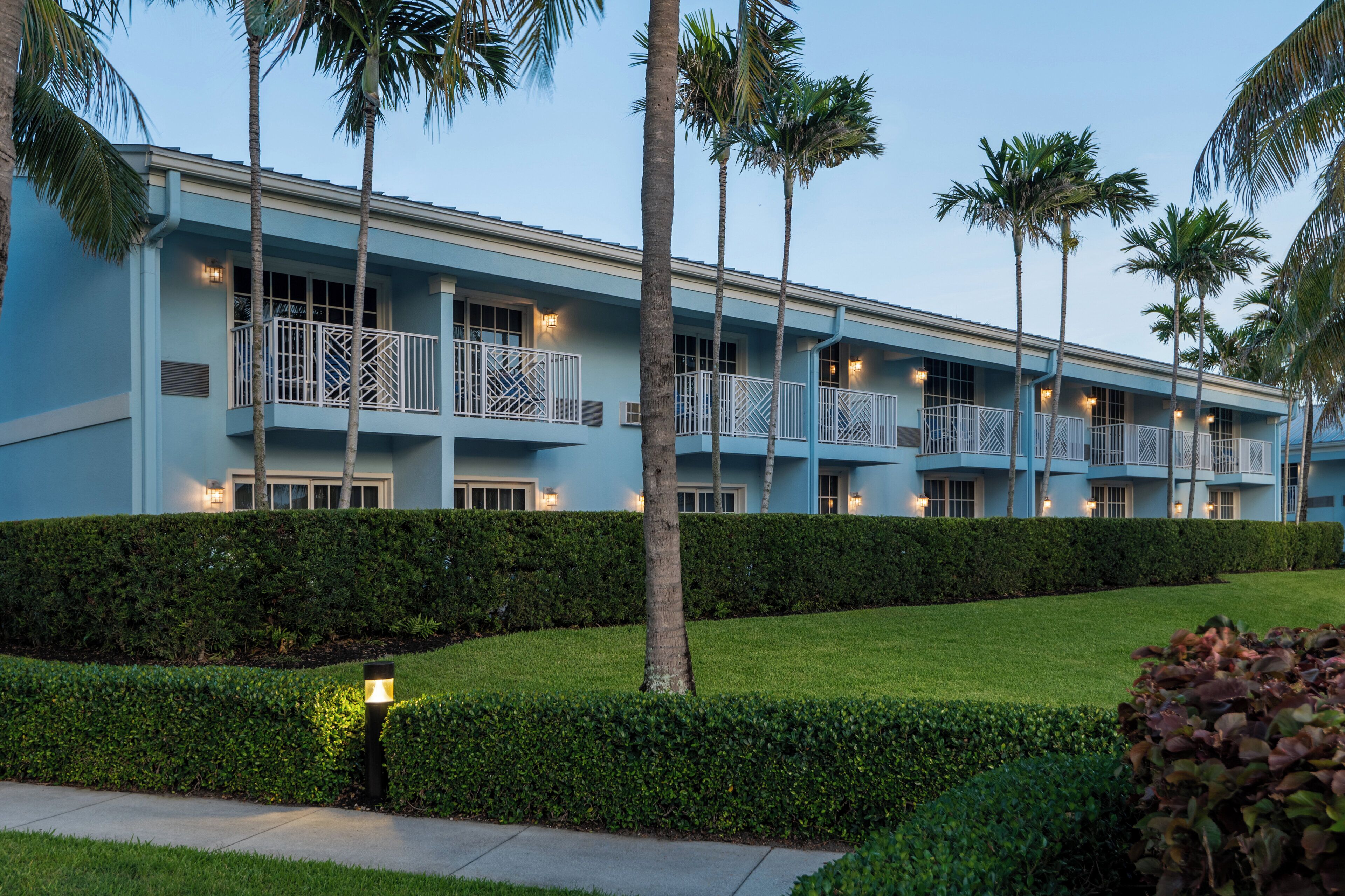 Un hotel con varios balcones, palmeras y setos cuidados.