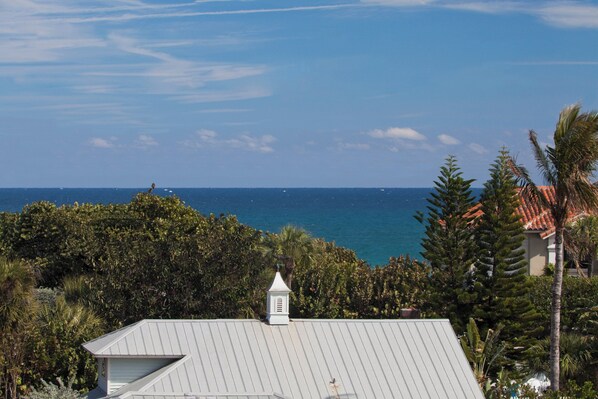 A coastal property with a view of the ocean, surrounded by dense foliage and a building with a white roof.