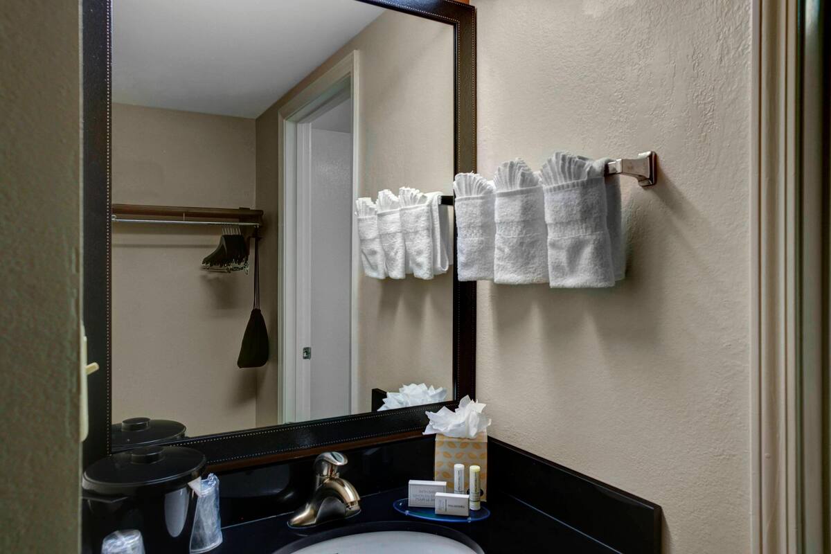 A bathroom with a sink, mirror, towel rack, and toiletries.