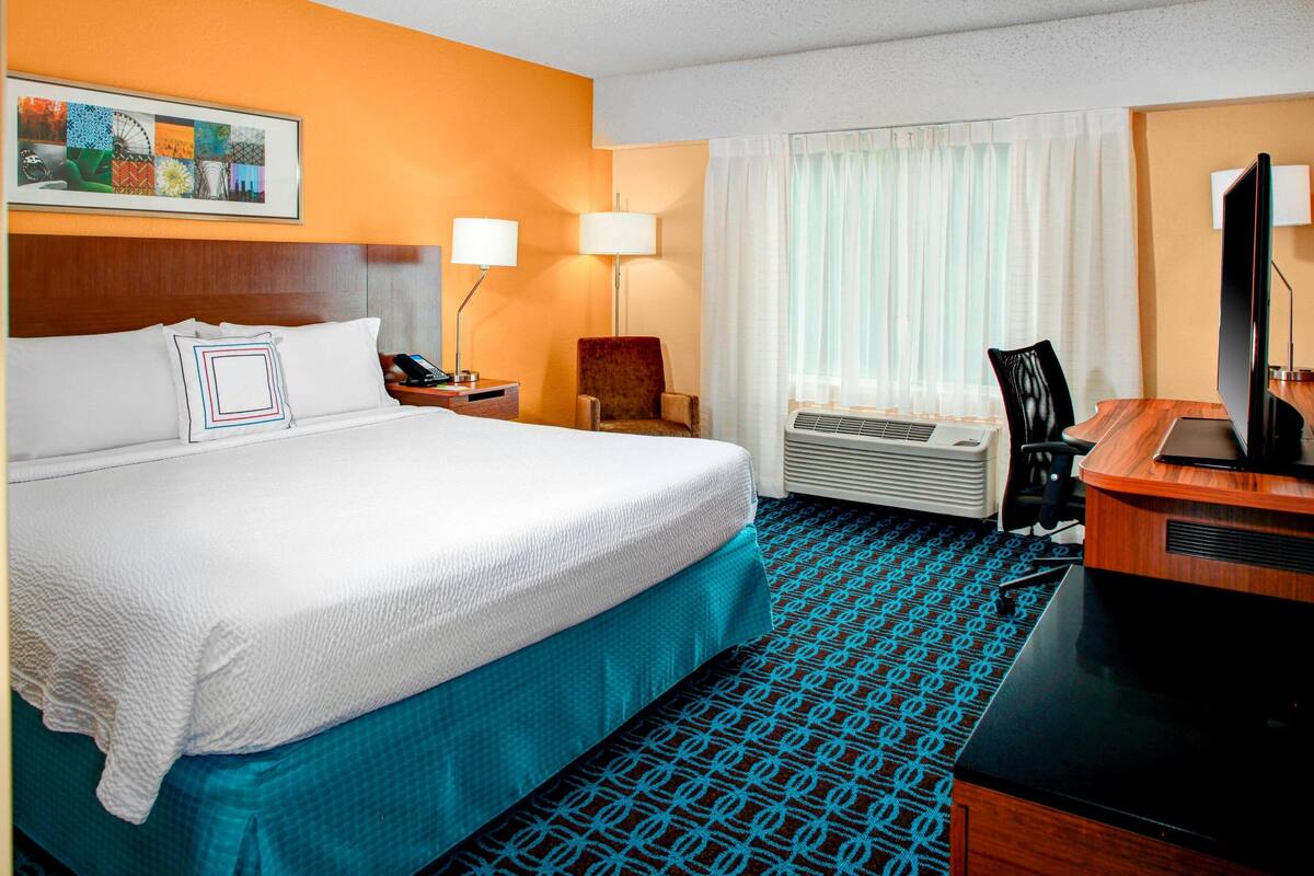 A hotel room with a large bed, two bedside lamps, a desk with a computer, and a window with curtains.