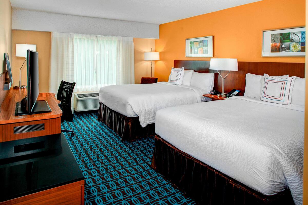 A hotel room with two beds, a desk, a television, and a patterned carpet.