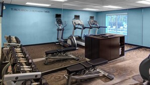 Ein Fitnessraum mit Laufbändern, Kurzhanteln und einer Trainingsbank.