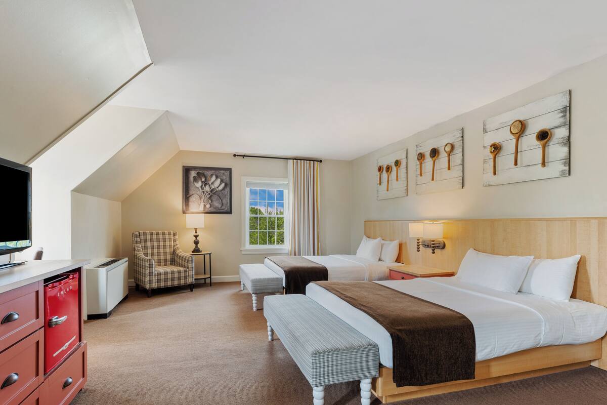 A hotel room with two beds, a TV, a chair, a desk, and artwork on the wall.