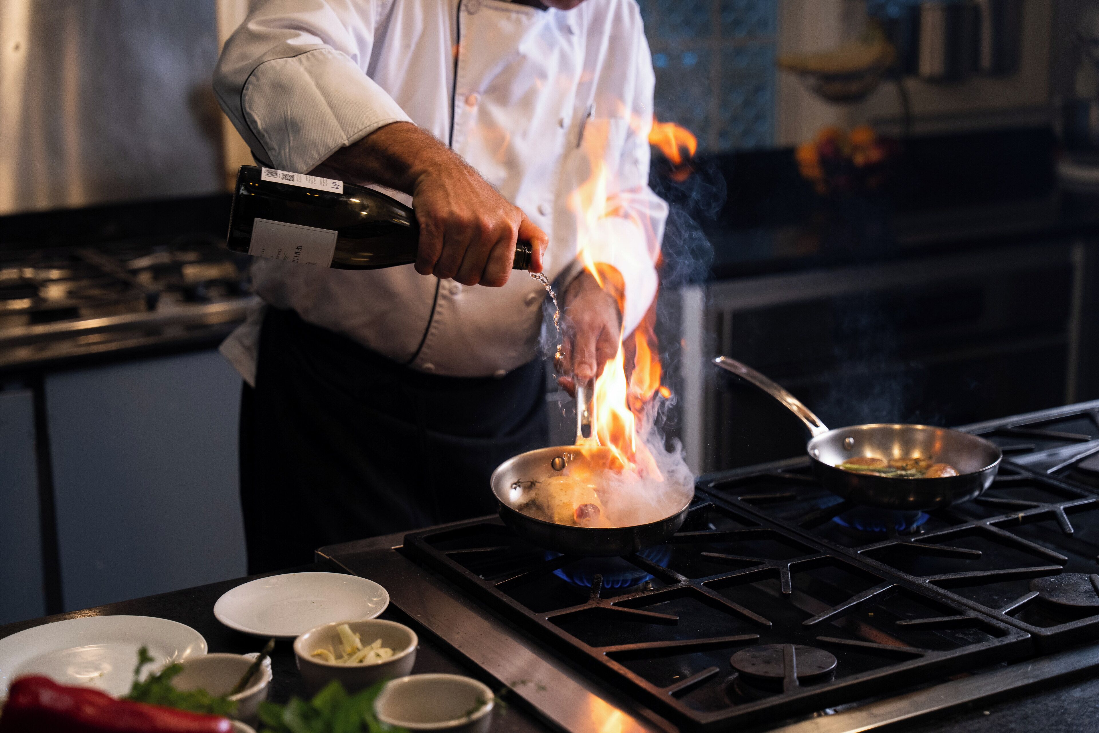 A chef cooking with flames on a stove, a pan, and a bottle of wine.