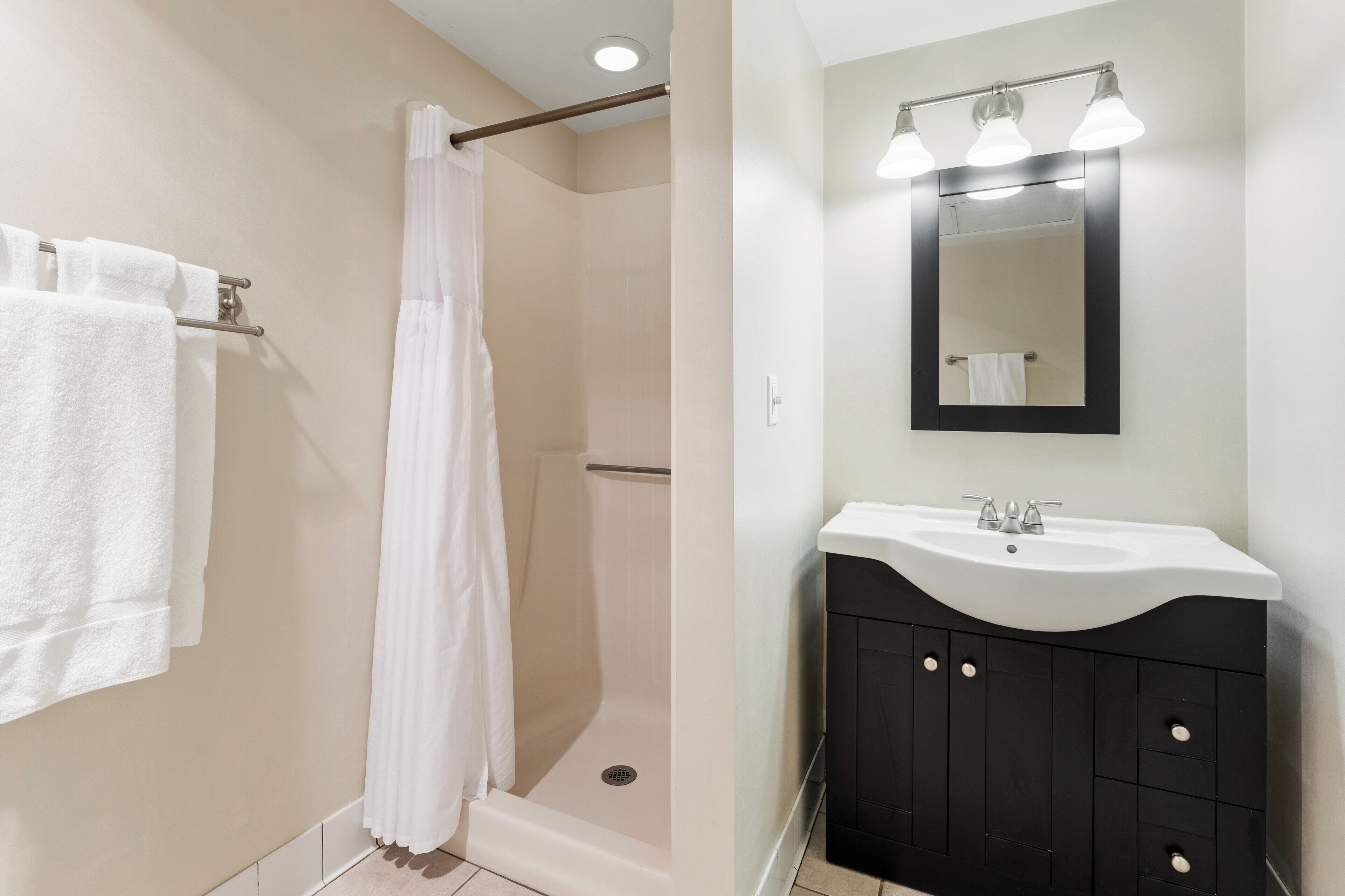 Un baño con ducha, lavabo con espejo y perchero.