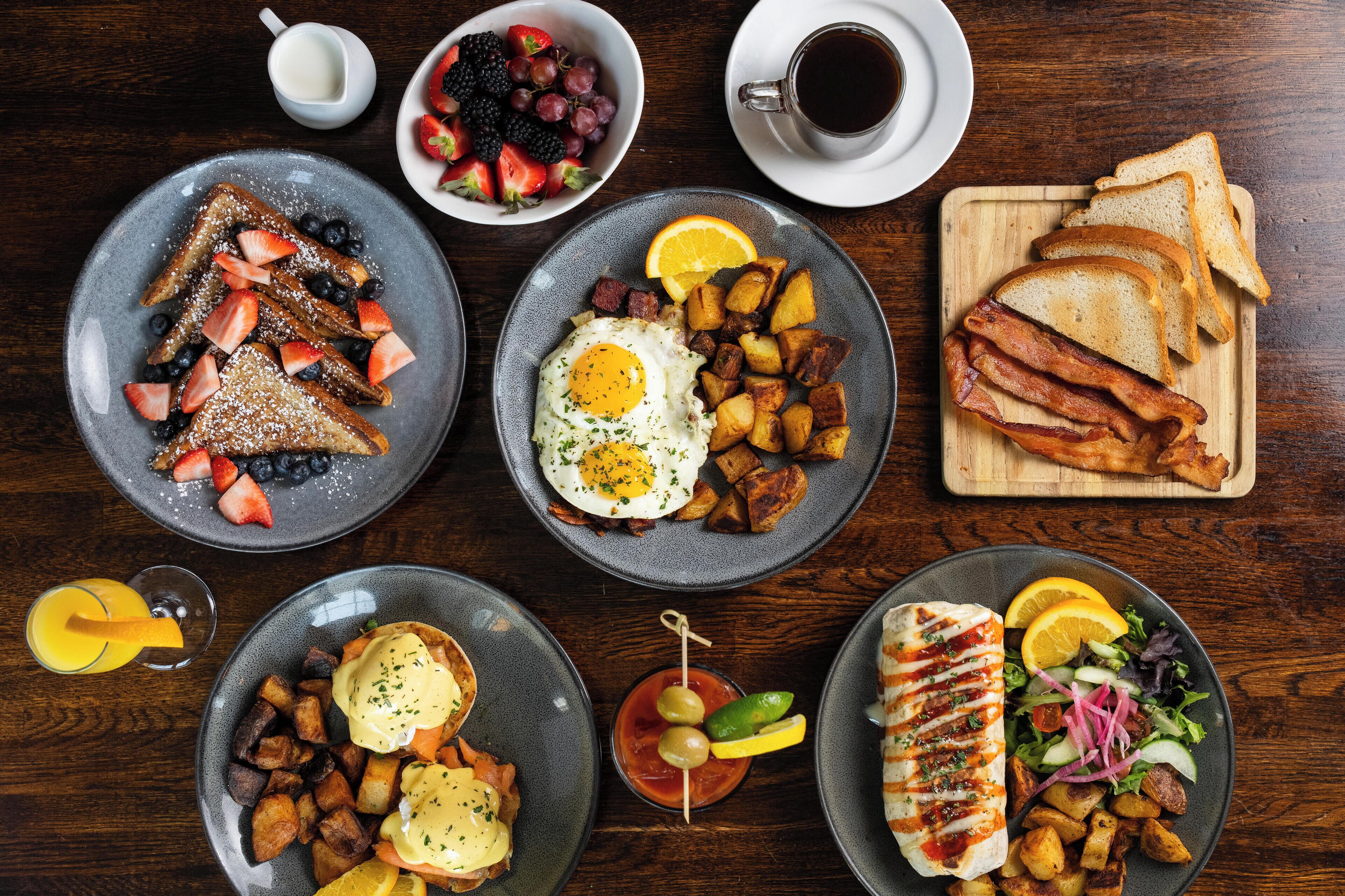 A breakfast spread with toast, eggs, bacon, and various fruits and vegetables on plates.