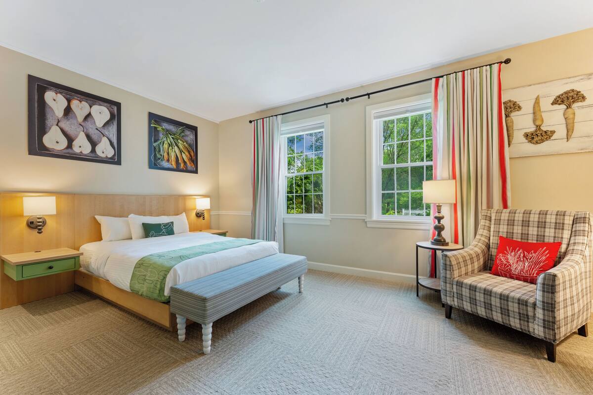 A bedroom with a bed, bedside tables, a chair, a window with curtains, and wall art.