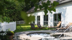 Patio trasero con un jacuzzi, dos sillas reclinables y una valla blanca.