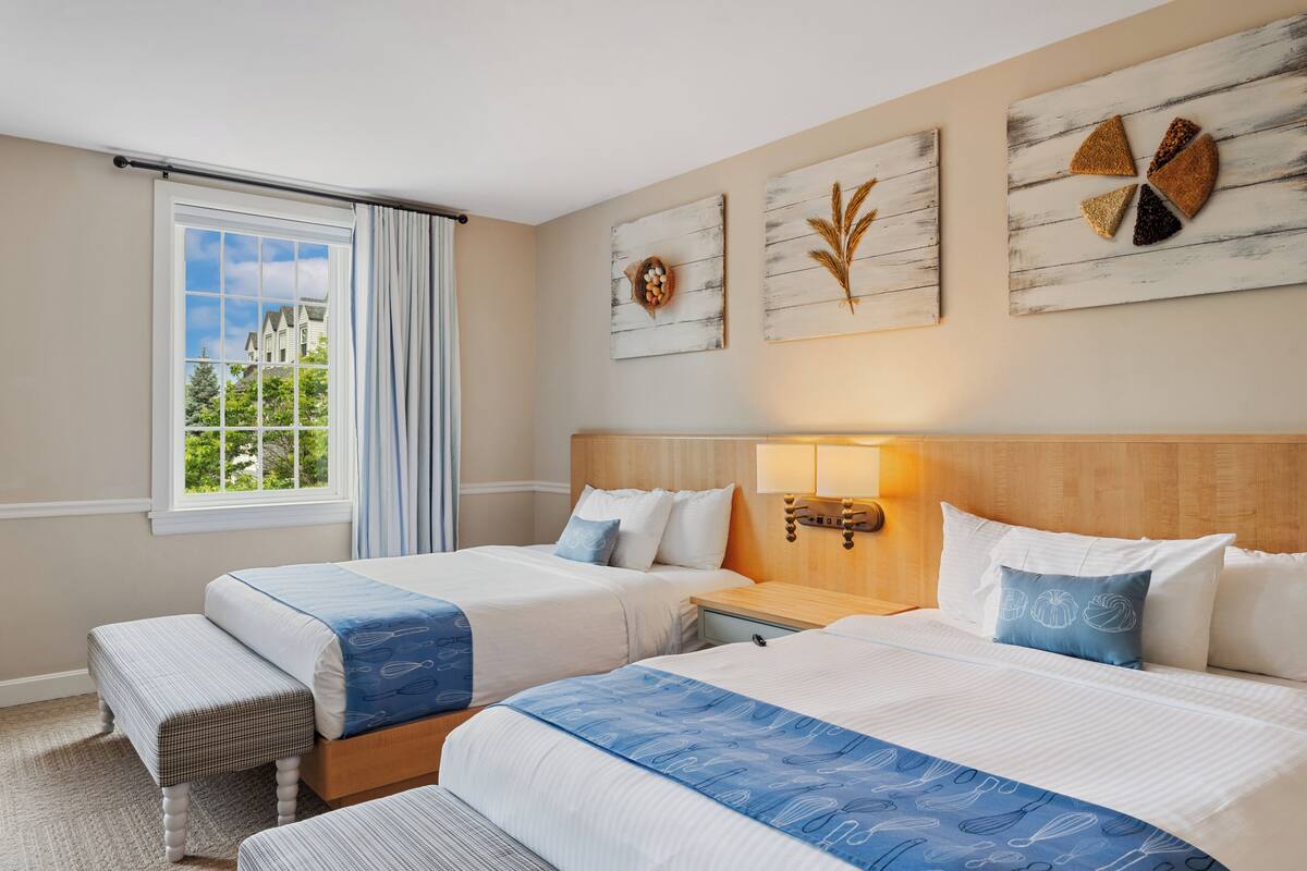 A hotel room with two beds, a window with curtains, a wooden headboard, and wall art.
