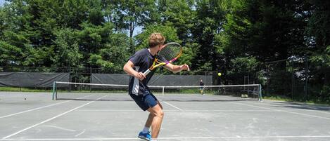 A tennis court with a net, surrounded by trees.