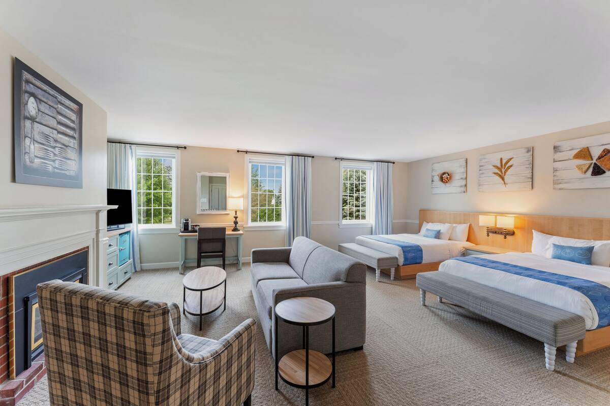 A hotel room with a fireplace, a sofa, a bed, a desk, and a chair.
