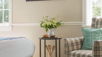 A bedroom with a bed, a chair, a small table with a vase of flowers, and a wall-mounted painting.