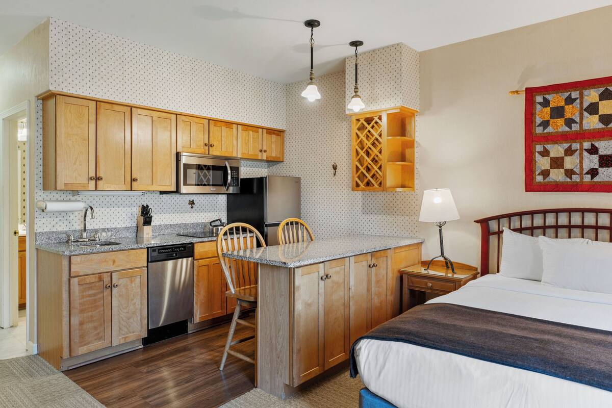 A compact hotel room with a kitchenette, a bed, and a small sitting area.