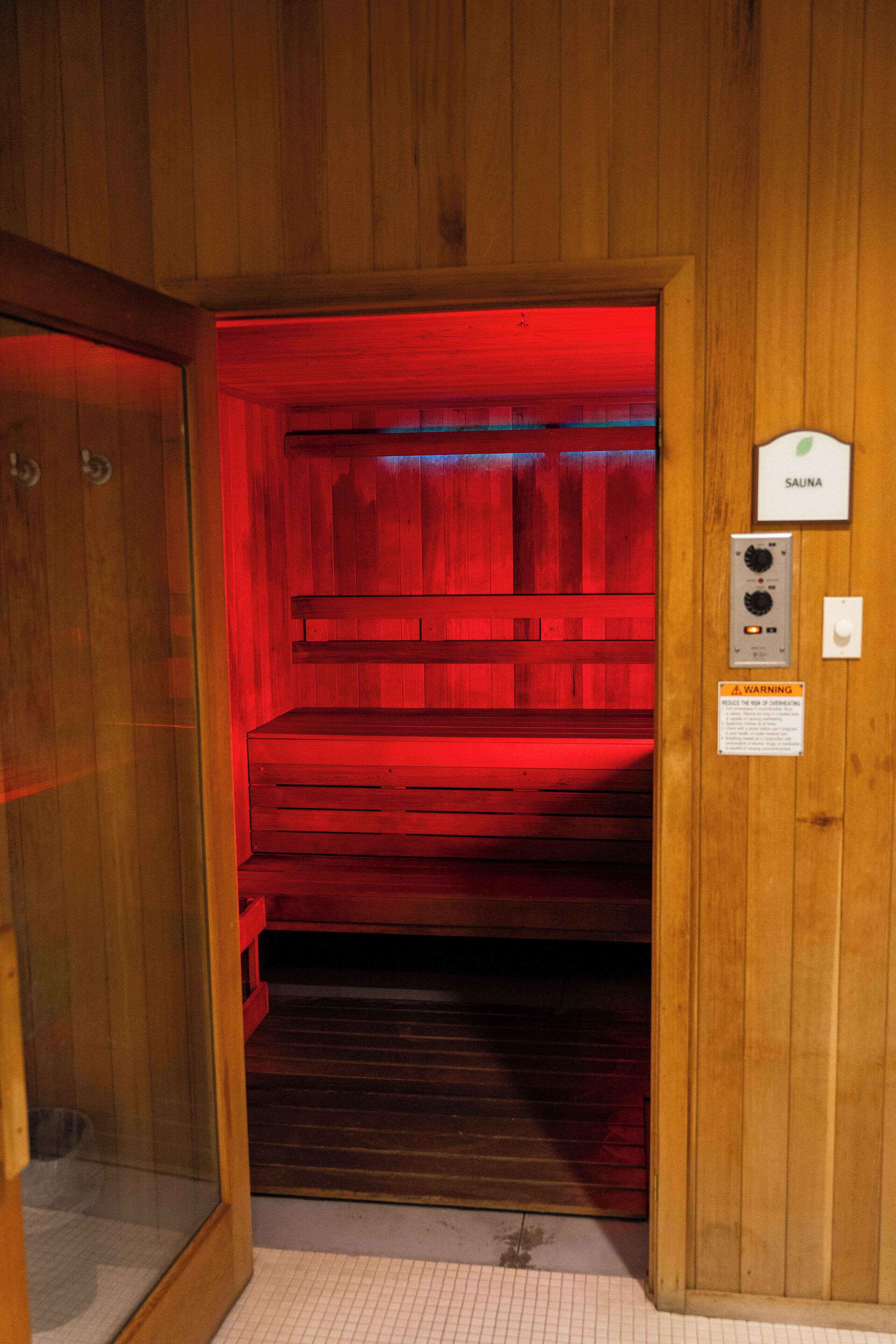 A sauna room with wooden walls and a red light. There is a sign indicating the room is a sauna.