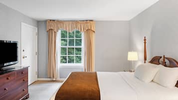 Habitación de hotel con cama, televisión, cómoda, ventana con cortinas y mesita de noche con lámpara.