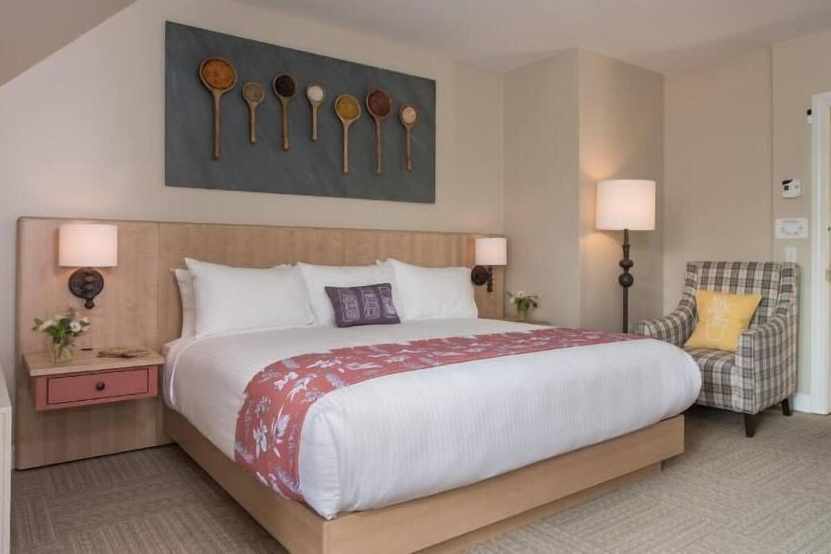 A hotel room with a large bed, two bedside tables, a chair, a wall-mounted artwork, and a door.
