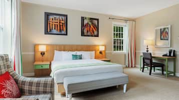 A hotel room with a large bed, a desk, a chair, and a bench.
