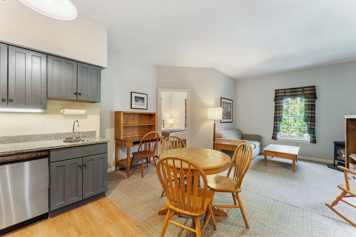 A modern kitchen with grey cabinets, a dishwasher, and a dining area with wooden chairs and a round table.
