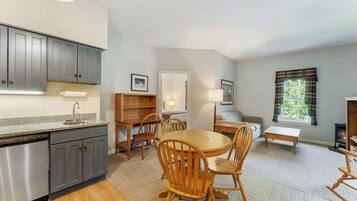 A modern kitchen with grey cabinets, a dishwasher, and a dining area with wooden chairs and a round table.