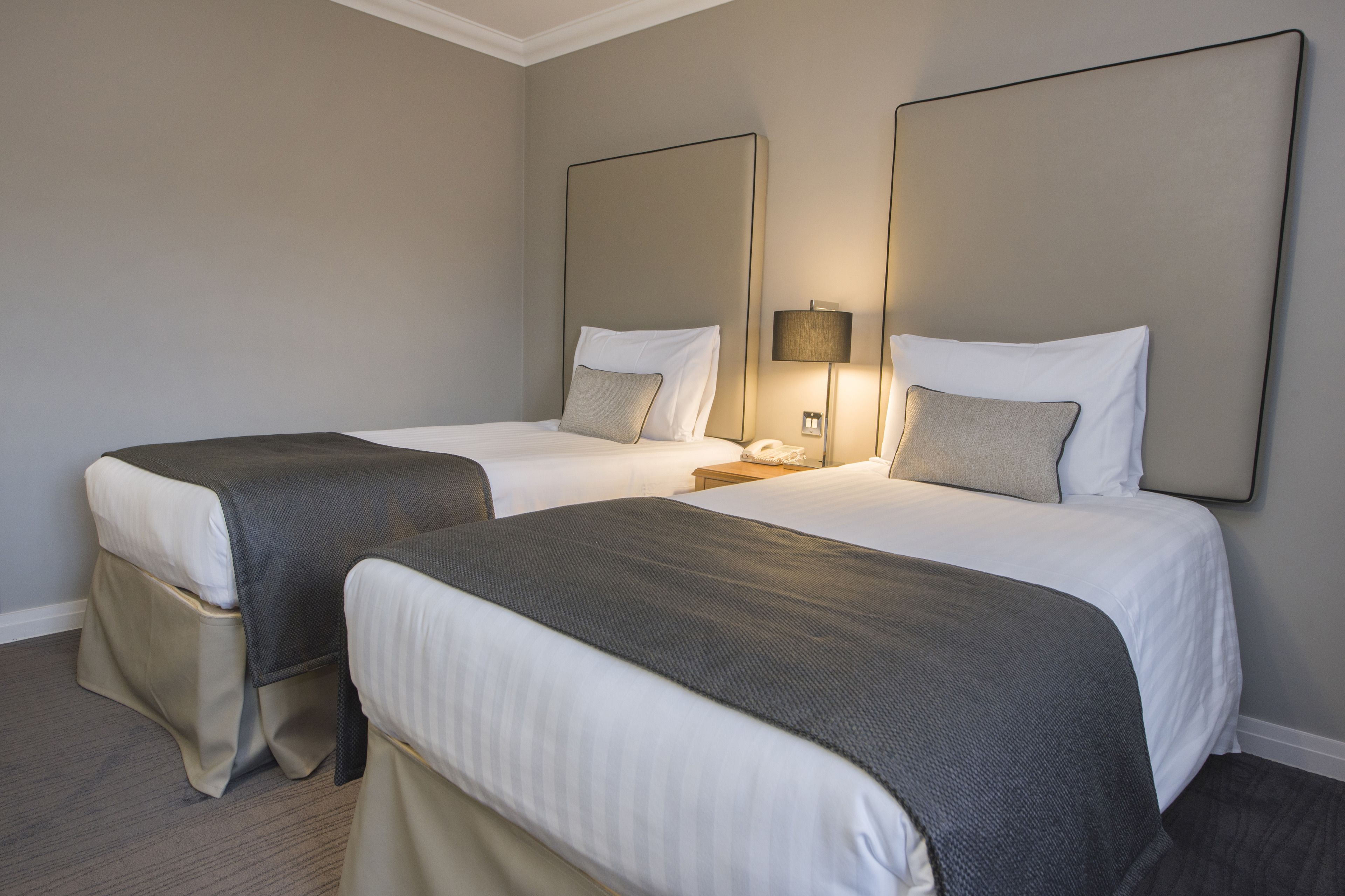 A hotel room with two beds, a nightstand with a lamp, and a large mirror on the wall.