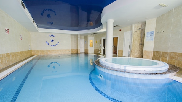 Une piscine intérieure dotée d’un jacuzzi, de murs carrelés et d’un plafond au motif circulaire.
