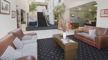 A hotel lobby with a staircase, two leather sofas, a coffee table, and framed pictures on the walls.