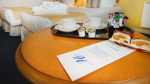 Une chambre d’hôtel avec un lit, une table de chevet sur laquelle se trouve un plateau avec des articles pour le petit-déjeuner, et un mot posé sur la table.