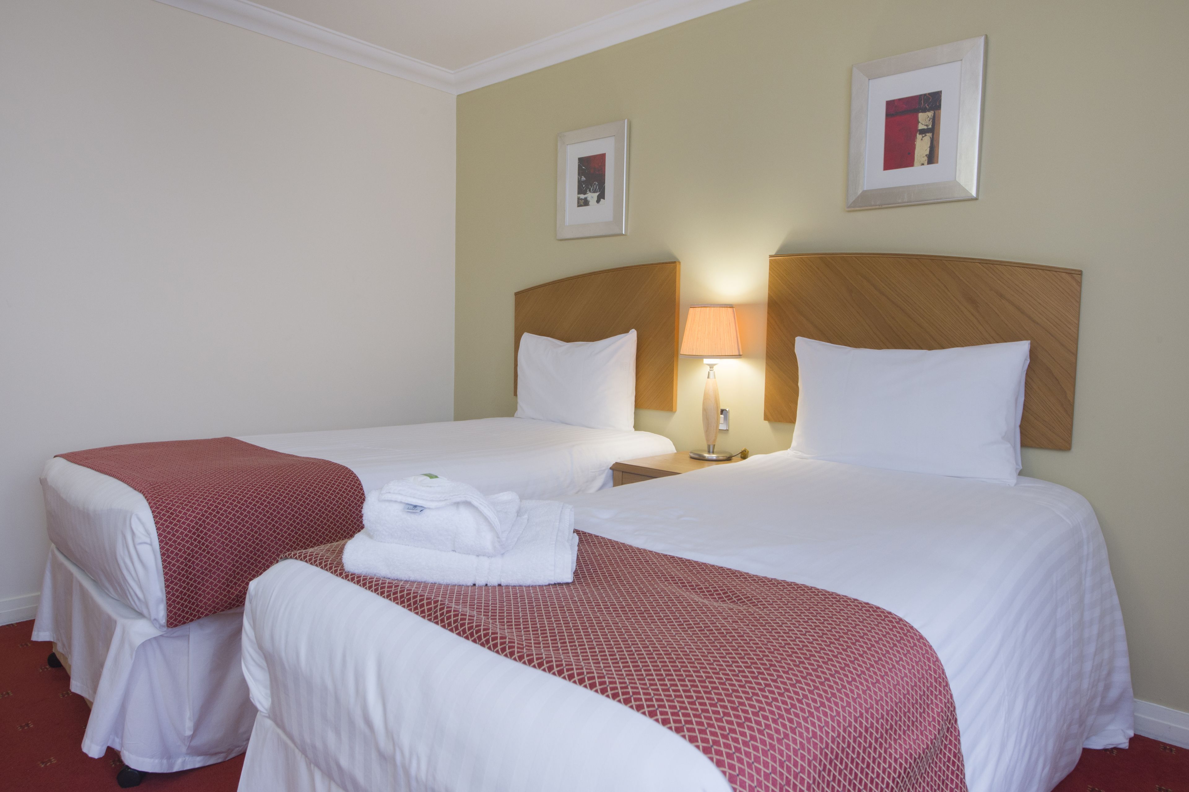 A hotel room with two beds, a nightstand with a lamp, and two framed pictures on the wall.