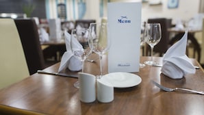 Une table à manger dressée avec un menu, des verres à vin, des assiettes et des couverts.