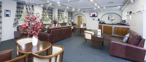 A hotel lobby with a reception desk, seating area, and a television screen.