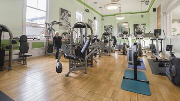 Un gimnasio con equipo de ejercicio variado, pisos de madera y ventanas amplias.