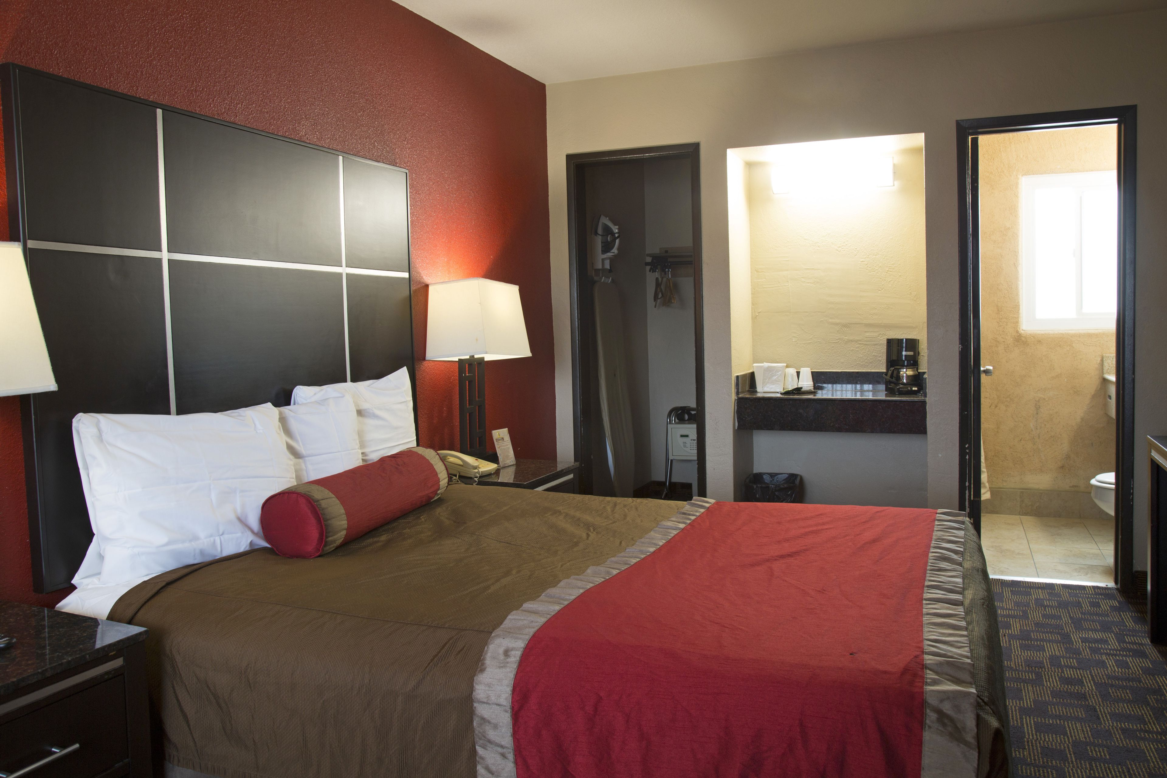 A hotel room with a bed, bedside tables, a lamp, a telephone, a mirror, and a bathroom visible through an open door.