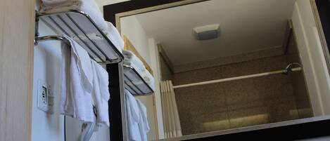 A bathroom with a large mirror, a towel rack with folded towels, and a shower area.