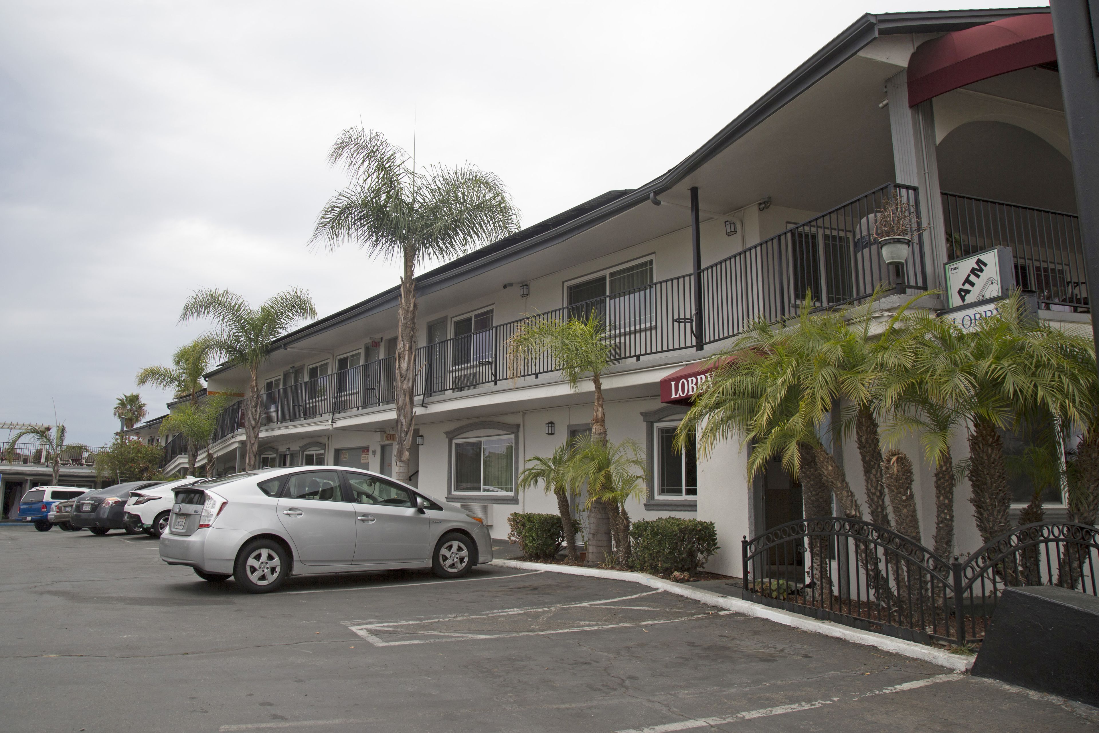 A hotel with a parking lot, a white car parked in front, and palm trees.