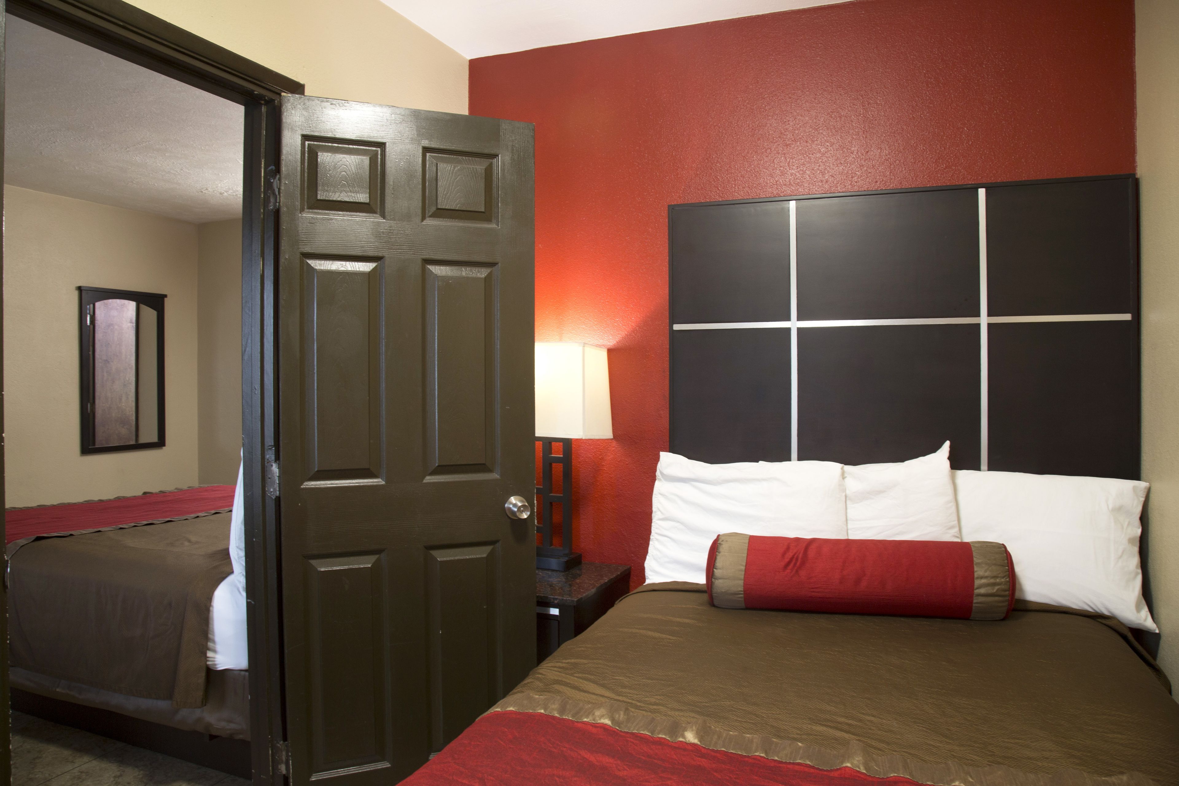 A hotel room with a large bed, a nightstand with a lamp, and a door leading to another room.