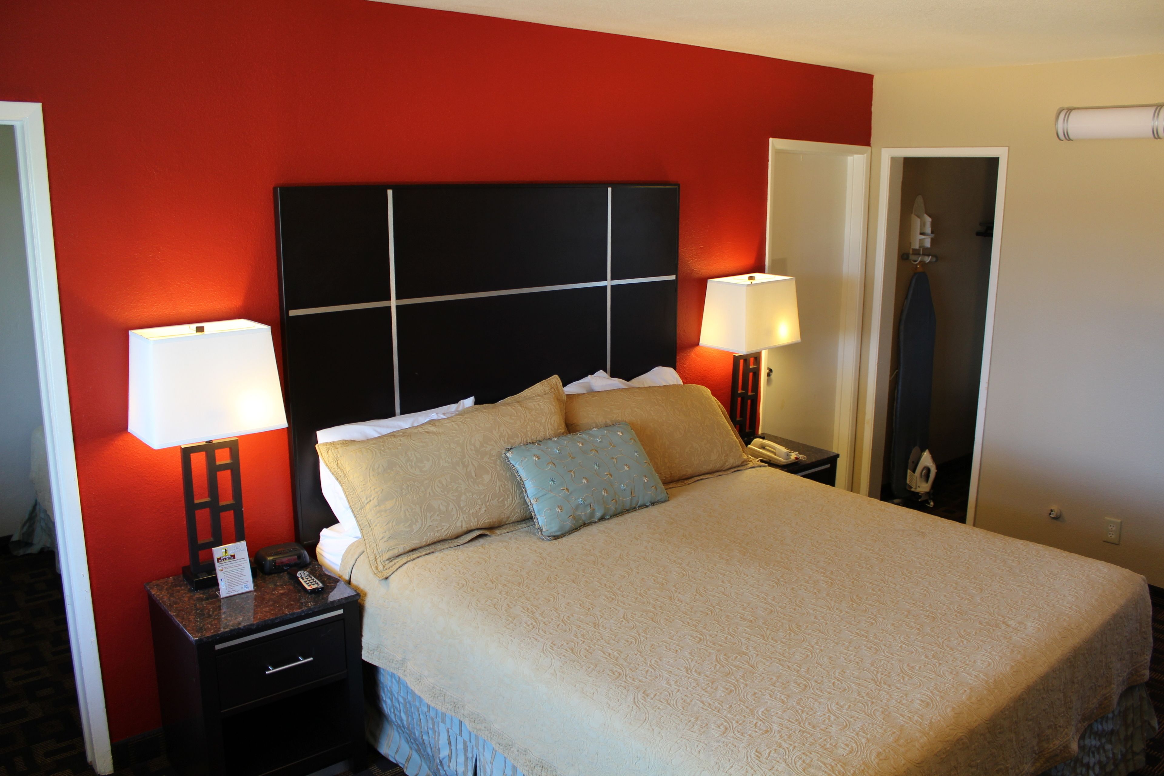 Habitación de hotel con una cama grande, dos mesitas de noche con lámparas, una pared de acento roja y una puerta que da al baño.