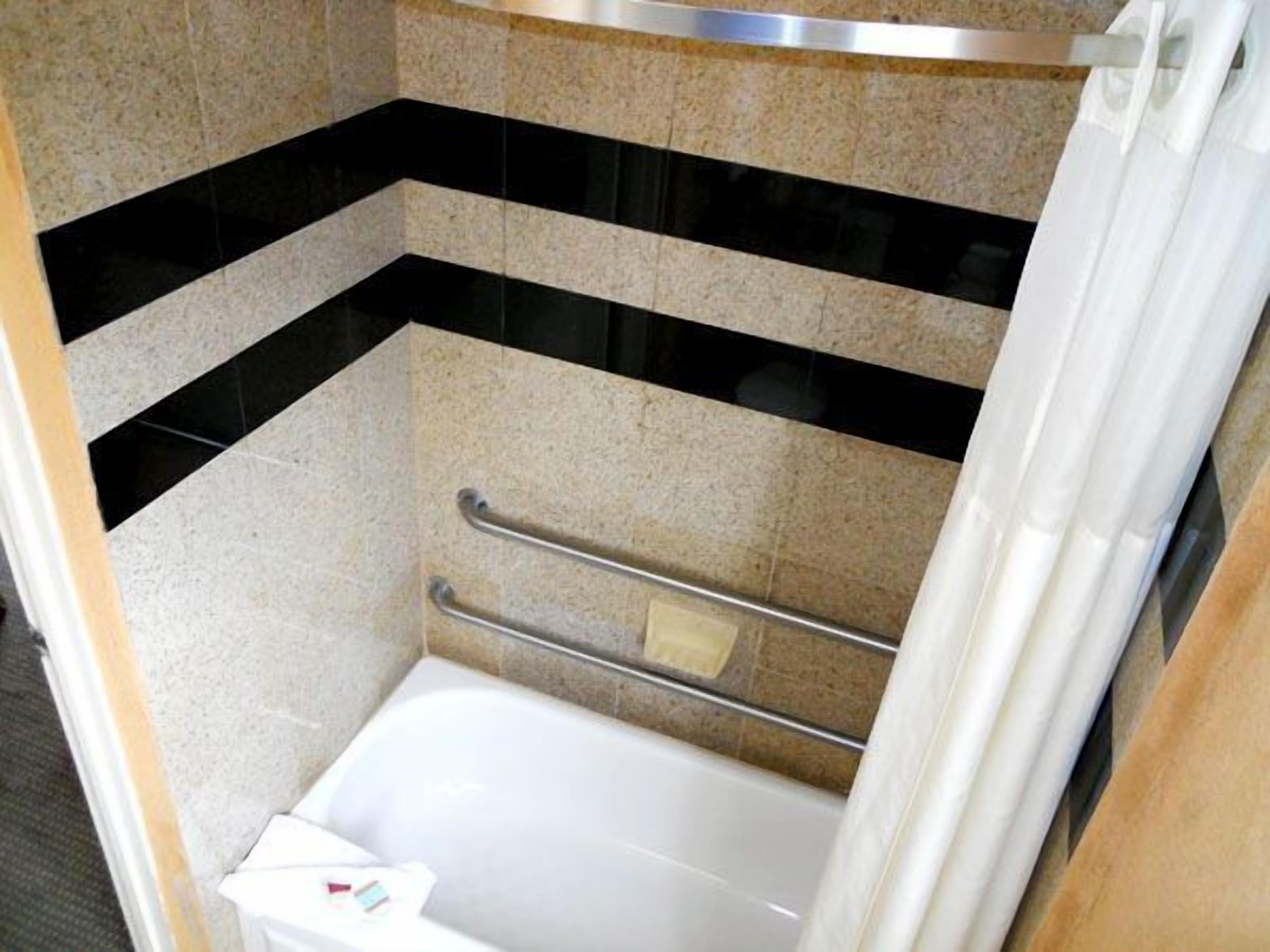Un espacio de ducha pequeño y cerrado con bañera, barra de apoyo y perchero.